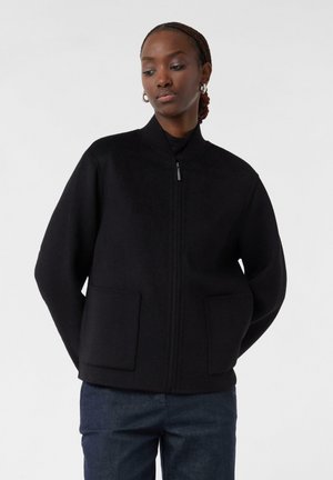 Schwarze Zip-Jacke aus weichem Stoff mit geripptem Kragen. Verfügt über zwei frontale Taschen und eine lockere Passform für mehr Komfort.