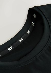 Tricou sport negru cu decolteu rotund, realizat dintr-un material neted și cu o etichetă branduită în interiorul gulerului, pe care este imprimat "self." alb.