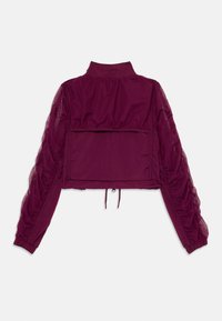 Casaco curto roxo com mangas transparentes franzidas, gola alta, aba de bolso traseiro e barra ajustável com cordão.