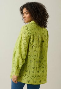 Camicia verde a maniche lunghe con motivi ritagliati e disegni floreali, polsini abbottonati e vestibilità rilassata. Tessuto testurizzato e cuciture dettagliate.