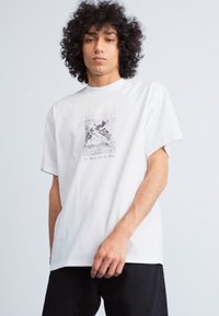 Hvid bomuld t-shirt med et centralt grafisk print i sort og grå. Rund halsudskæring, korte ærmer og afslappet pasform.