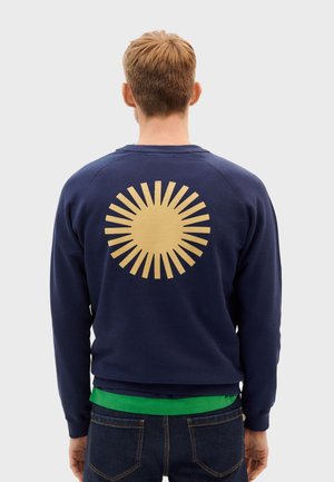 Navy sweatshirt with a gold sunburst graphic on the back. Features ribbed cuffs and hem, soft texture, and a relaxed fit.