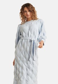 Hellblaues, gestricktes Kleid mit einem strukturierten Rautenmuster, langen Ärmeln und einem passenden Gürtel in der Taille. Es hat einen runden Ausschnitt.