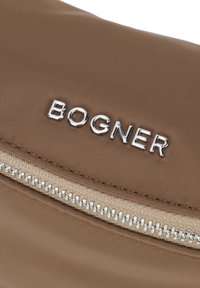 Borsa in nylon marrone con un logo argento "BOGNER" e una cerniera beige con denti metallici, che mostra una texture liscia e linee pulite.