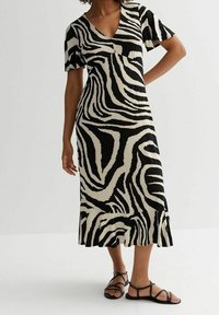 Mustavalkoinen seepra-kuosinen mekko, jossa lyhyet hihat, V-päänti ja levenevä helma. Päällä tasaiset mustat sandaalit. Kangas on sileä ja pehmeä.