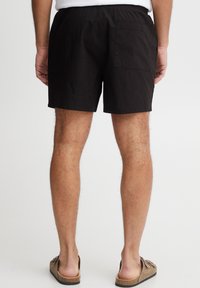 Mustadest puuvillast lühikesed püksid elastse vöökohaga, ühe tagatasku ja lamedate õmblustega, koos pruunide hõõrutuslõpmistega. Minimalistlik disain.