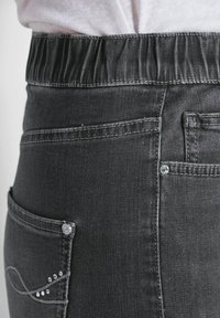 Dunkelgraue Denim-Hosen mit einem gesammelten elastischen Bund, auffälliger Naht und dekorativen Akzenten auf der Gesäßtasche.