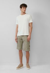 Witte crewneck T-shirt voor heren, olijfgroene cargoshorts met zijzakken, en beige sneakers met een gestructureerde bovenkant en rubberen zolen.