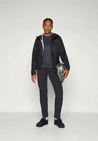 Svart vanntett jakke med grå detaljer, grå skjorte, mørke bukser og svarte sko. Holder en grå sykkelhjelm.