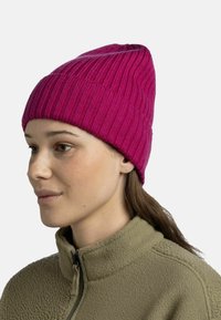 Pink knit beanie with vertical ribbed texture, tapering shape. Worn with a textured olive green fleece top featuring a high collar.