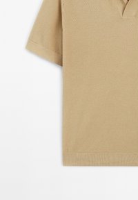 Polo a maniche corte in beige con un motivo a nido d'ape testurizzato, caratterizzato da un collo a V e orli a coste sulle maniche e in fondo.