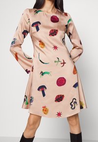 Šaty do délky kolen s dlouhým rukávem z měkké broskvové látky, zdobené barevnými abstraktními vzory zahrnujícími houby, listy a ovoce.