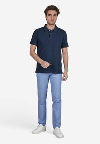 Marineblauwe polo met korte mouwen, twee knopen bij de kraag. Lichtblauwe broeken, slim fit, gecombineerd met witte sneakers. Eenvoudig design.