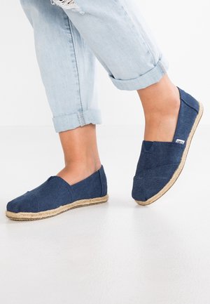 Voeten met blauwe canvas instappers met touwzolen, gecombineerd met lichtblauwe opgerolde spijkerbroeken.