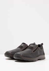 Zwarte instappers van leer met elastische zijpanelen, contrasterende stiksels en textuur rubberen zolen. Rond neusontwerp.