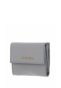 Portefeuille compact en cuir gris clair avec logo doré "COCCINELLE" et finition texturée, design plié avec surpiqûres visibles.