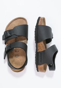 Svarta sandaler med två justerbara spännen, korkfotbädd och texturerad gummisula; släta läderremmar; avslappnad design med öppen tå.