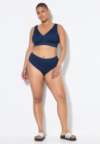 Tmavě modrý texturovaný bikini set s braletkou s výstřihem do V a vysokými kalhotkami. Doplněno černými skluznými sandály s bílými akcenty.