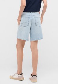 Bermudas de denim azul claro con un ajuste relajado, diseño de cinco bolsillos y detalles de costura visibles, combinadas con zapatillas beige.