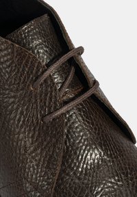 Bruine leren schoen met een gestructureerd oppervlak, vetersluiting met donkerbruine veters en een gladde afwerking op de neus.