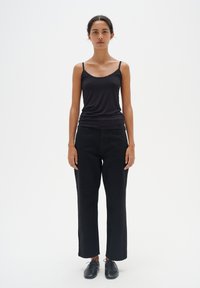 Top nero senza maniche con spalline sottili, abbinato a pantaloni neri larghi e scarpe nere stringate. Texture liscia, design semplice.