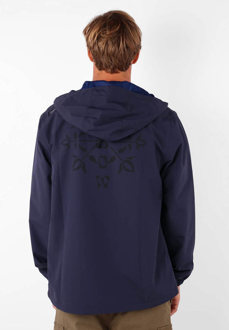 Veste imperméable marine avec capuche, présentant un motif floral noir au dos, des manches longues et un design simple et élégant.