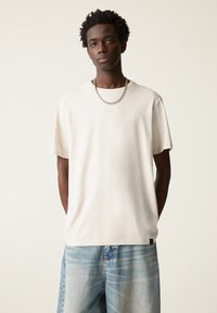 Lys beige bomulds t-shirt med korte ærmer, rund hals, afslappet pasform og subtil tekstur, parret med falmede blå buksestil med brede ben.