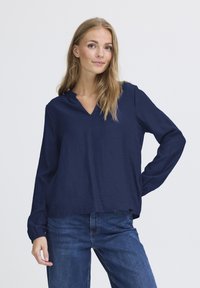 Maglietta a maniche lunghe blu navy con scollatura a V e una trama sottile. Vestibilità comoda con orlo dritto, abbinata a jeans di denim blu.