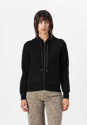 Zwarte zip-up hoodie met een capuchon met trekkoord, voorzien van een gladde textuur en voorzakken, gecombineerd met beige broek met luipaardprint.