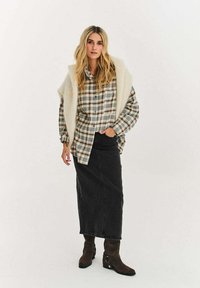 Kostkovaná košile zapínaná na knoflíky v béžové, zelené a hnědé barvě, doplněná dlouhou černou džínovou sukní. Zdůrazněno krémovým texturovaným šálem a hnědými botami.