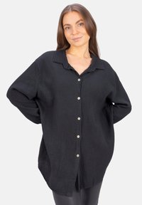 Black button-up shirt in textured fabric, featuring a collar, long sleeves, and a slightly oversized fit with side slits.