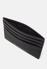 Étui à cartes en cuir noir avec plusieurs fentes pour cartes, extérieur texturé et détail de logo subtil à l'avant. L'intérieur est doublé de tissu.