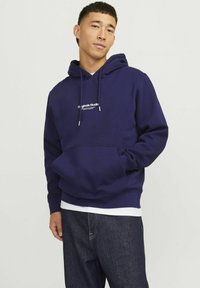 Felpa con cappuccio blu navy in misto cotone, dotata di tasca a marsupio e coulisse. Presenta un logo bianco sul petto e polsini a coste.
