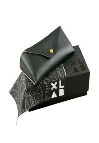 Svart läderfodral med rundad klaff och guldtryckknapp, placerad på en svart låda med vita geometriska mönster och logotyp.