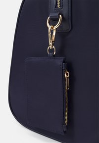 Marinblå axelväska med detaljer i guldton och en liten dragkedjefodral, tillverkad av ett glatt och hållbart tyg.