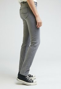 Jean denim gris à coupe slim, avec des poches standards et une texture subtile légèrement délavée, associé à des baskets montantes noires.