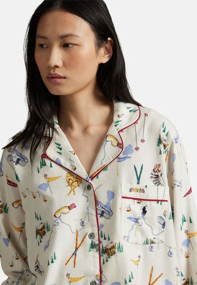 Parte superior de pijama con tela color crema con un estampado colorido de temática al aire libre, ribetes rojos y un bolsillo en el pecho. Botones al frente.