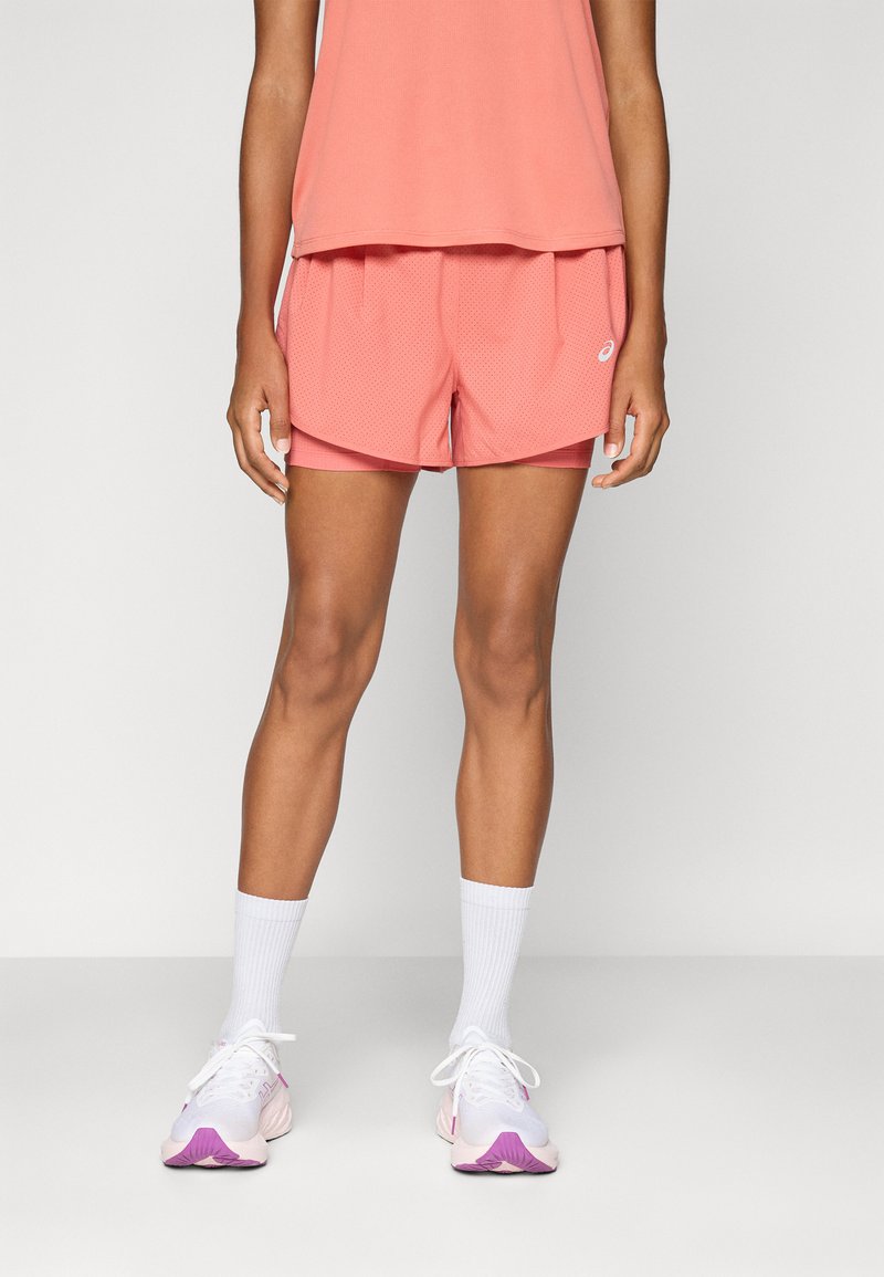 Top de manga corta en color coral combinado con pantalones cortos de malla coral ligeros. Calcetines blancos hasta la mitad de la pantorrilla y zapatillas blancas con acentos rosas completan el look.