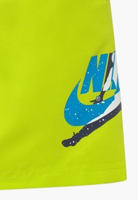 Pantalones cortos deportivos de color verde neón con un logotipo de Nike en azul y negro, con un diseño horizontal y textura suave.