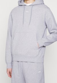 Sudadera de algodón gris con un bolsillo canguro, capucha con cordón y puños acanalados. Logotipo impreso en el pecho, acompañada de pantalones de chándal a juego.