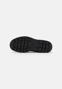 Suela de sneaker de goma negra con surcos profundos, forma redondeada y superficie texturizada. Presenta marcas de marca y tamaño en el arco.