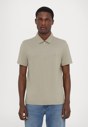 Polo-shirt i lys olivengrøn bomuld med lynlåskrave og korte ærmer; har et lille broderet logo på venstre bryst.