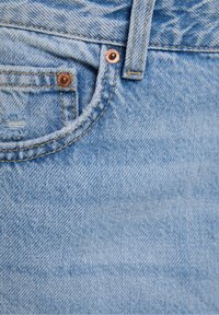 Primo piano di un tessuto di denim azzurro chiaro che mostra una piccola tasca frontale, un passante per cintura, rivetti e una texture indossata con dettagli di cucitura.