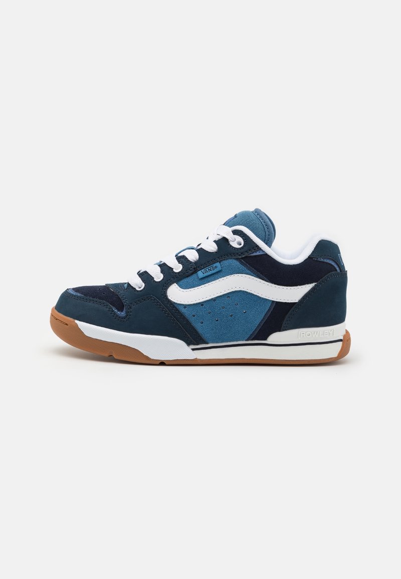 Tenisky s modrým semišovým a síťovaným svrškem, bílými tkaničkami a hnědou gumovou podrážkou. Mají charakteristický swoosh a perforované detaily.