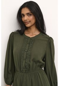 Olive green dress made of soft fabric, with a round neckline, button closure, lace detailing, and voluminous puff sleeves.