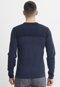Marineblå genser med strukturstrikk, rund hals, lange ermer og ribbede mansjetter. Glatt bakpaneldetalj.
