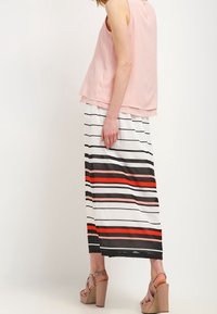 Haut sans manches rose clair associé à une longue jupe rayée avec des lignes horizontales noires, blanches et rouges. Sandales à talons épais.