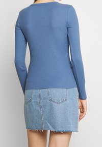 Maglia a maniche lunghe a coste in blu morbido, abbinata a una mini gonna in jeans chiari con orlo sfrangiato e tasche posteriori. Design semplice e aderente.