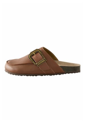 Brązowe skórzane półbuty wsuwane z szerokim paskiem i dużą prostokątną klamrą. Podeszwa ma fakturę dla lepszej przyczepności.