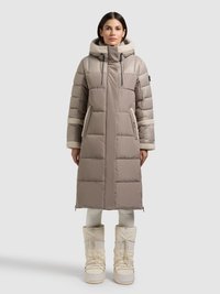 Parka acolchada beige con capucha forrada de piel sintética, cremallera frontal, bolsillos laterales y diseño hasta la rodilla, combinada con botas de nieve blancas.